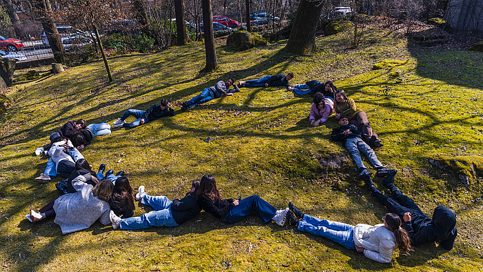 Jugendliche formen auf einer Wiese liegend ein Herz