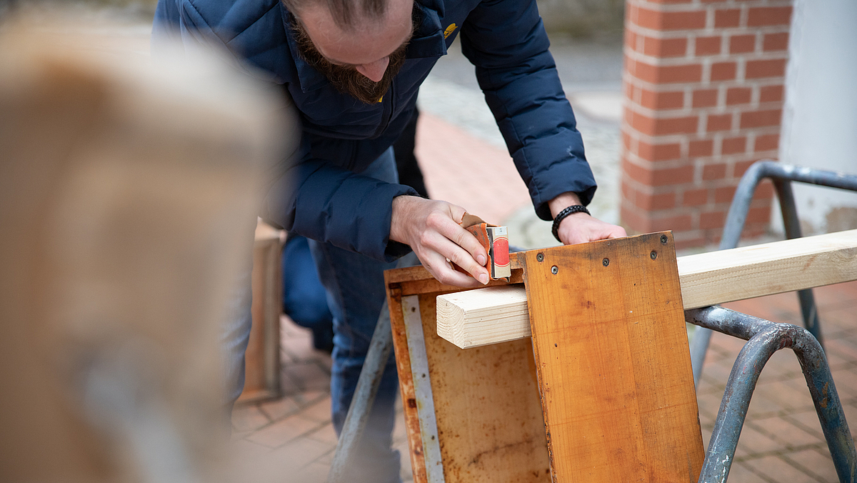 Ein Mann in Winterjacke schleift mit der Hand eine Holzbeute.