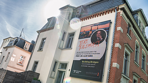 Hoher Besuch: Alar Karis, estnischer Staatspräsident, kommt in die Hochschulstadt. Brücken gibt es bereits. Sie sollen weiter gebaut werden. (Foto: Helmut Hammer) Eine Hausfassade mit einem wandfüllenden LED-Display: Es zeigt das Foto von Alar Karis und unter anderem den Text „Building Bridges“. Im gegen die Sonne gemachten Foto spiegeln sich die Linsen des Objektivs.