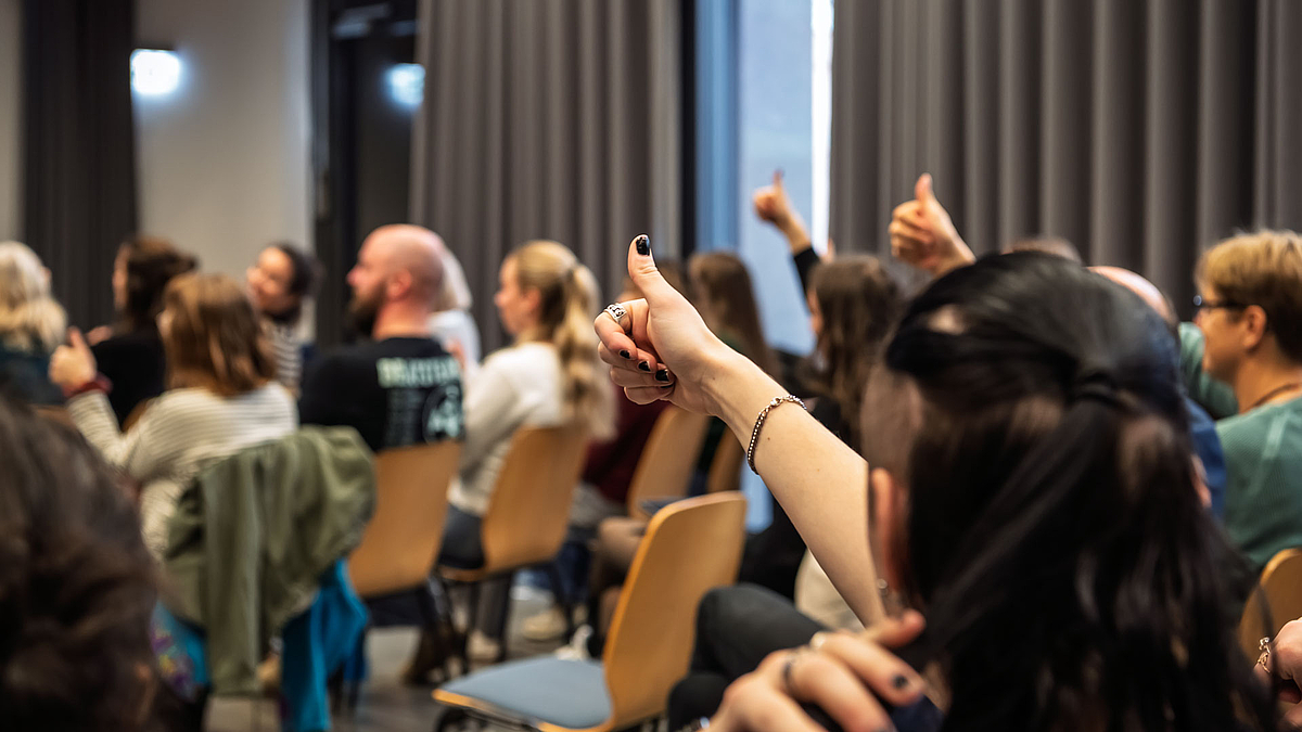 Blick von hinten auf Personen, die ihre Arme mit "Daumen hoch" nach oben stecken.