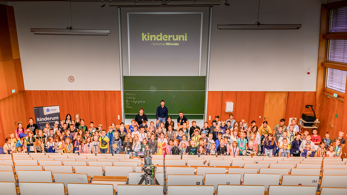 Gruppenfoto von oben im Hörsaal mit allen Kindern, dem Dozenten und dem Kinderuni-Team