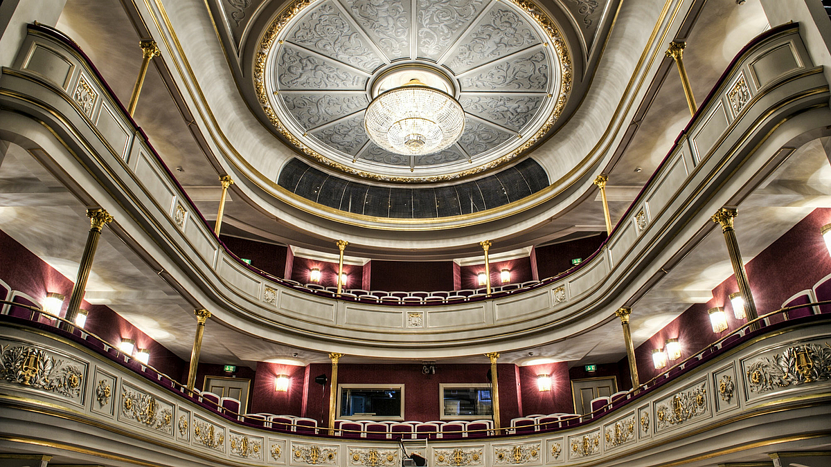 Das Foto zeigt reich verzierte Ränge und Decke des Zuschauerraums des Theaters von der Bühne aus fotografiert.