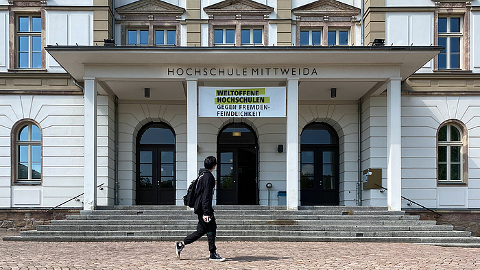 Das Portal zum Hauptgebäude der Hochschule Mittweida. Unter dem Schriftzug "Hochschule Mittweida" ist zwischen zwei Säulen hängt übetr den Treppenstufen ein Banner mit dem Text "Weltoffene Hochschulen gegen Fremdenfeindlichkeit".