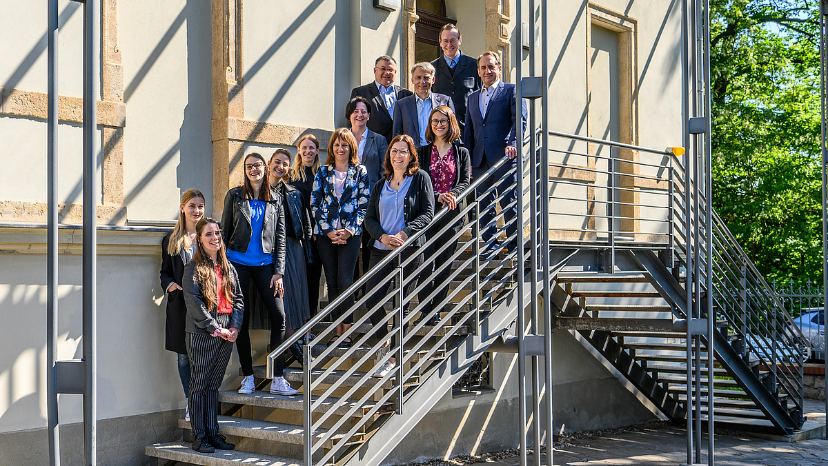 Das Gruppenfoto zeigt 13 Personen auf der metallenen Treppe zu einem historischen Gebäude.