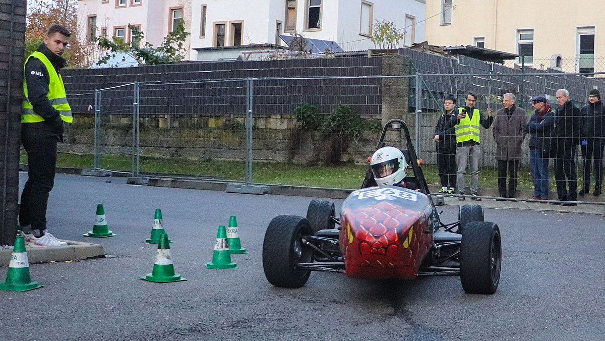 Rennauto fährt vor Zuschauenden im Hintegrund hinter Bauzäunen.
