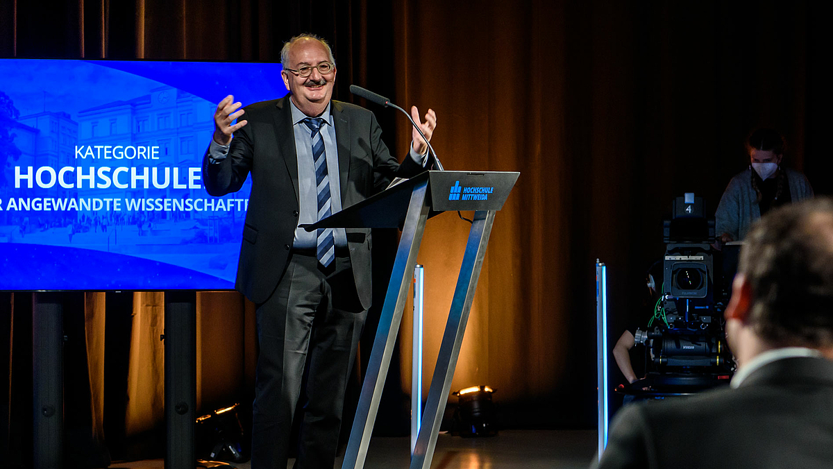 Auf dem Foto ist der Laudator für Marc Ritter, der Rektor der Hochschule Mittweida Ludwig Hilmer zu sehen. Unscharf im Bildvordergrund ist Marc von Ritter zu sehen.