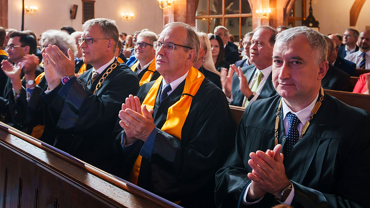 Mehrere Professoren applaudieren. Sie tragen Talare und sitzen auf Kirchenbänken in der Stadtkirche Mittweida.