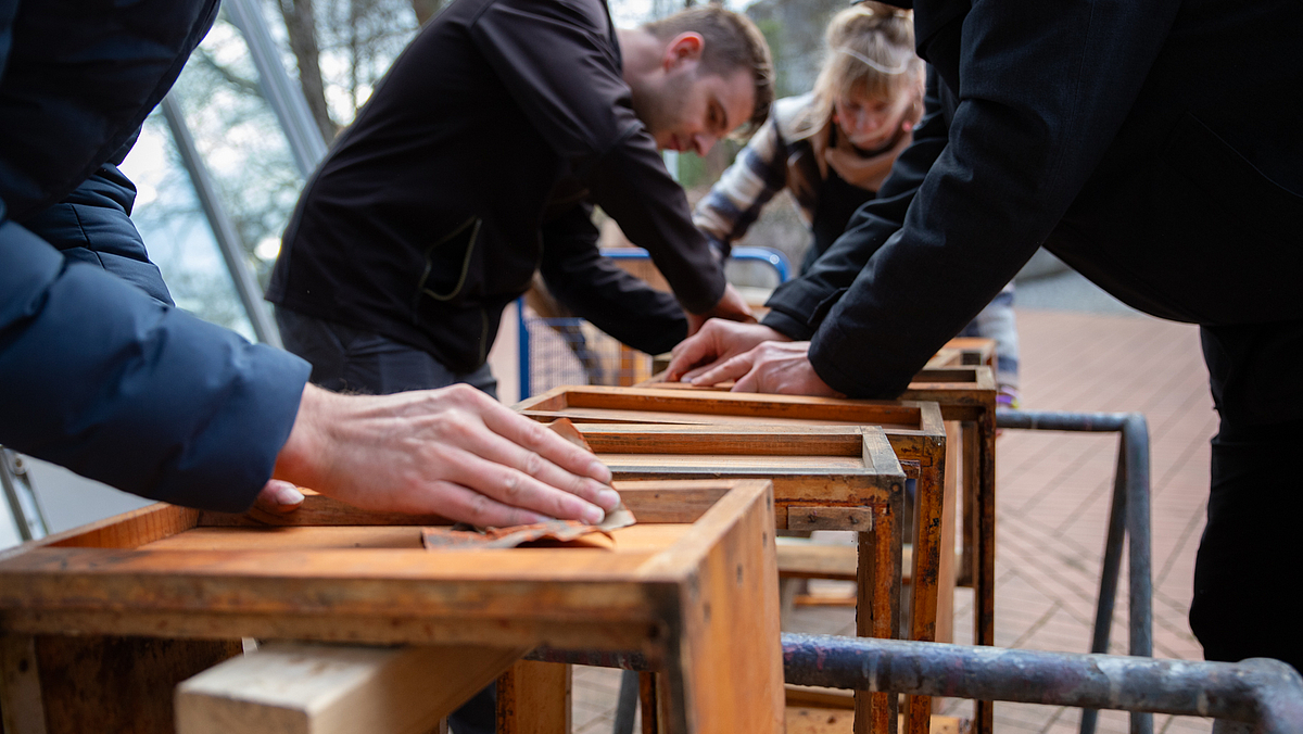 Vier Menschen schleifen Holzbeuten mit der Hand.