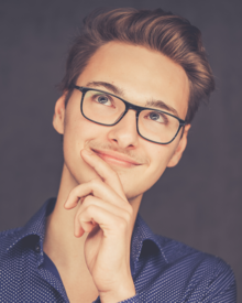 Moritz Schloms blickt lächelnd nach oben. Seine linke Hand hält er in "Denker-Pose" an sein Kinn.