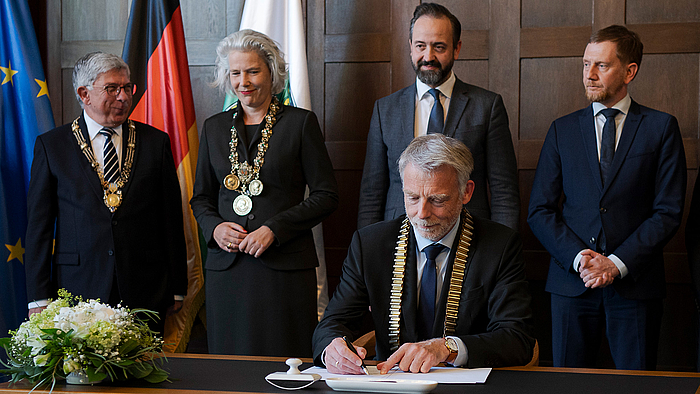 Rektor Volker Tolkmitt unterzeichnete die Zuschussvereinbarung für die Hochschule Mittweida am 14. Mai 2024 in Dresden. Volker Tolkmitt sitzt an einem Tisch und unterschreibt ein Stück Papier. Er trägt die Amtskette des Rektors der Hochschule Mittweida.