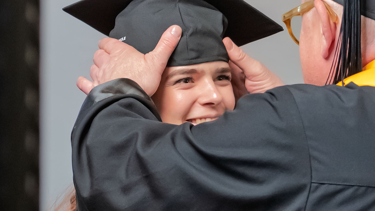 Professor im Talar setzt Absolventin Hut auf.