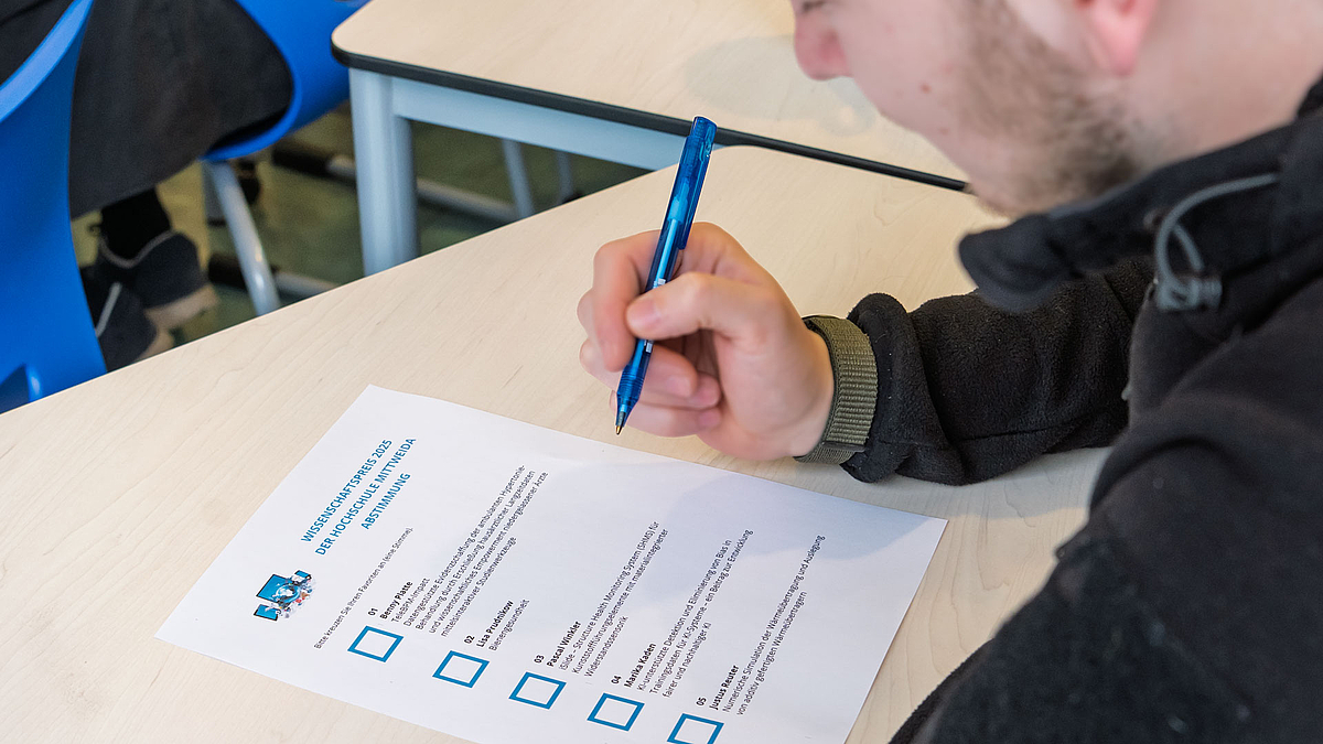 Blick auf eine männliche Person mit Kugelschreiber vor einem Stimmzettel mit fünf Wahlmöglickeiten.