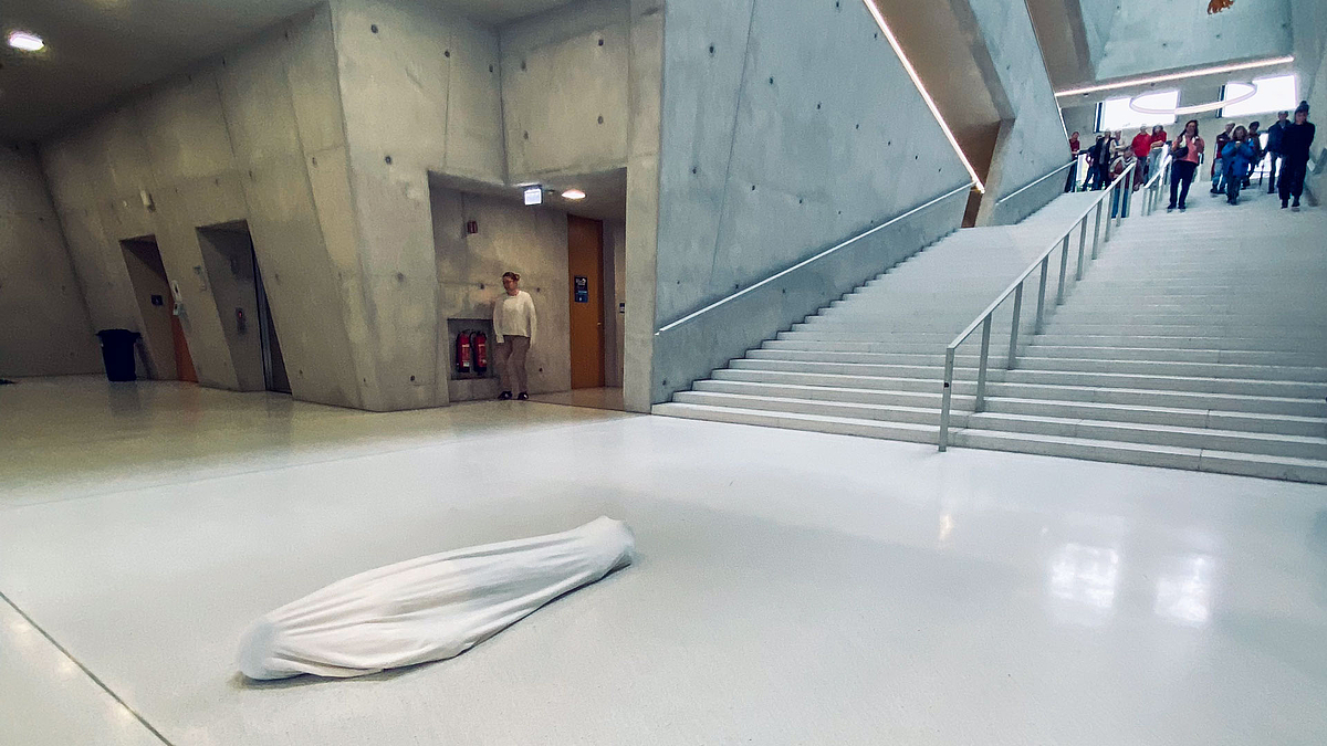 Im Foyer vor ineer großen Treppe leigt ein Körper in einen Leichensack eingehüllt.
