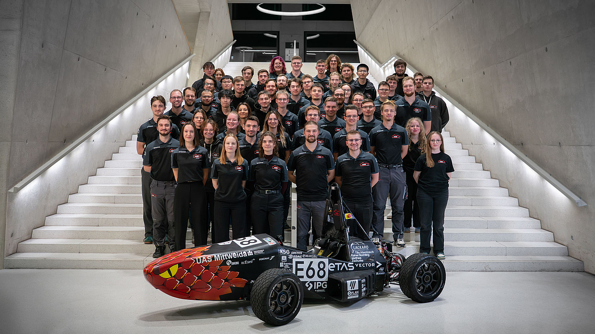 Gruppenfoto mitrund 50 jungen Personen auf einer großen Treppe und em Rennauto im Vordergrund.