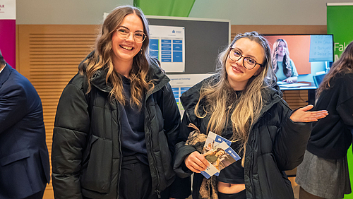 Zwei junge Frauen schauen lachend bzw. lächelnd in die Kamera