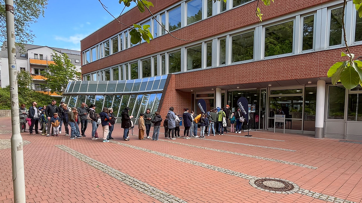 Kinder und Erwachsene in einer Schlange vor dem Eingang eines roten Backsteingebäudes