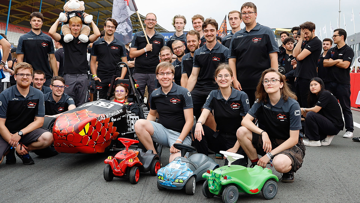Team aus 20 jungen Menschen, das Rennauto und drei Bobbycars.
