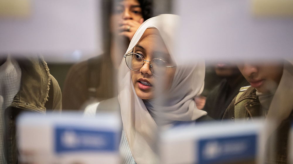 Junge Frau mit Kopftuich vor Flyerständer.