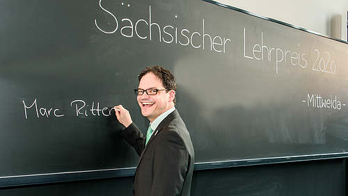 Das Fotos zeigt den Preisträger Marc Ritter, der gerade seinen Namen an die Kreidetafel eines Hörsaals gerschrieben hat.