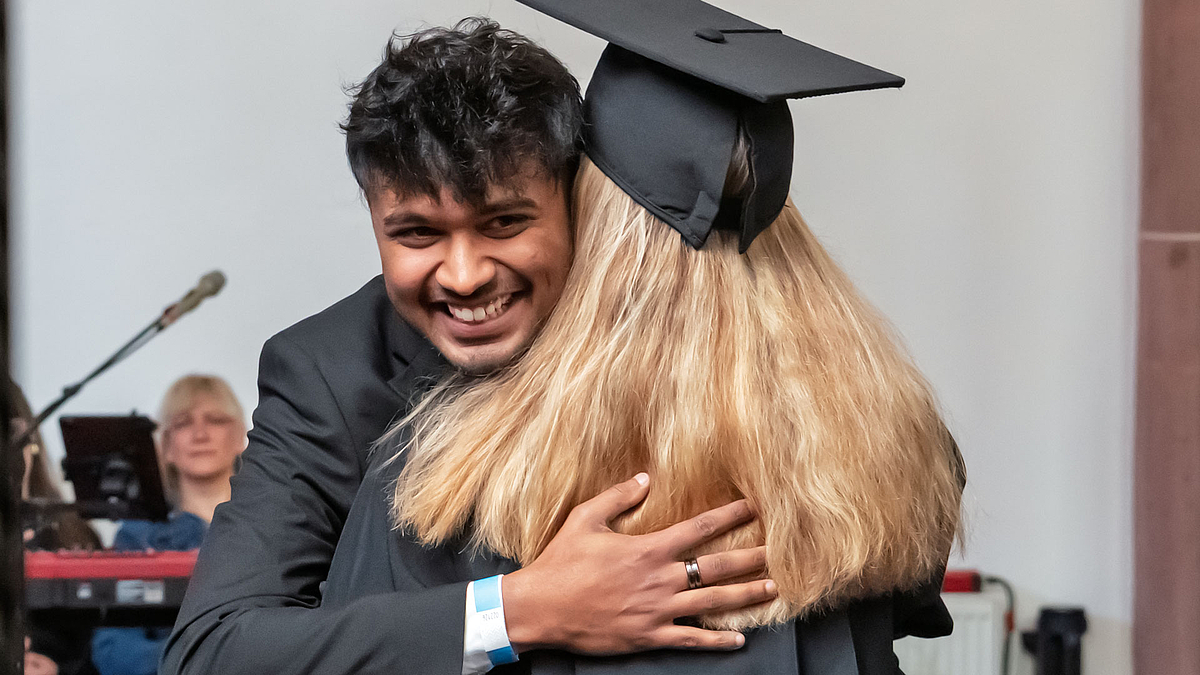 Absolvent noch ohen Hut umarmt herzlich Professorin im Talar