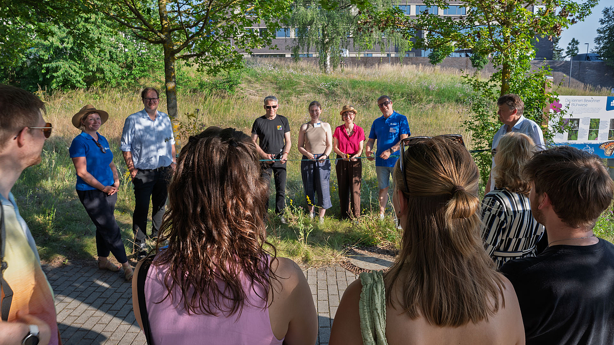 Den Weg zu Nachhaltigkeit und Biodiversität eröffnet: Professorin Anika Möcker, Kanzler Ulrich Pietsch, Rektor Volker Tolkmitt, Anika Lemm, Professorin Inga-Maria Eichentopf, Professor Ralf Hartig, Prorektor Christoph Meyer (v.l.n.r.). Memschen auf einer Wiese mit Schere hinter einem roten Band.