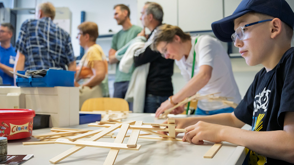 Ein Junge baut aus kleinen Holzlatten eine Brückenkonstruktion.