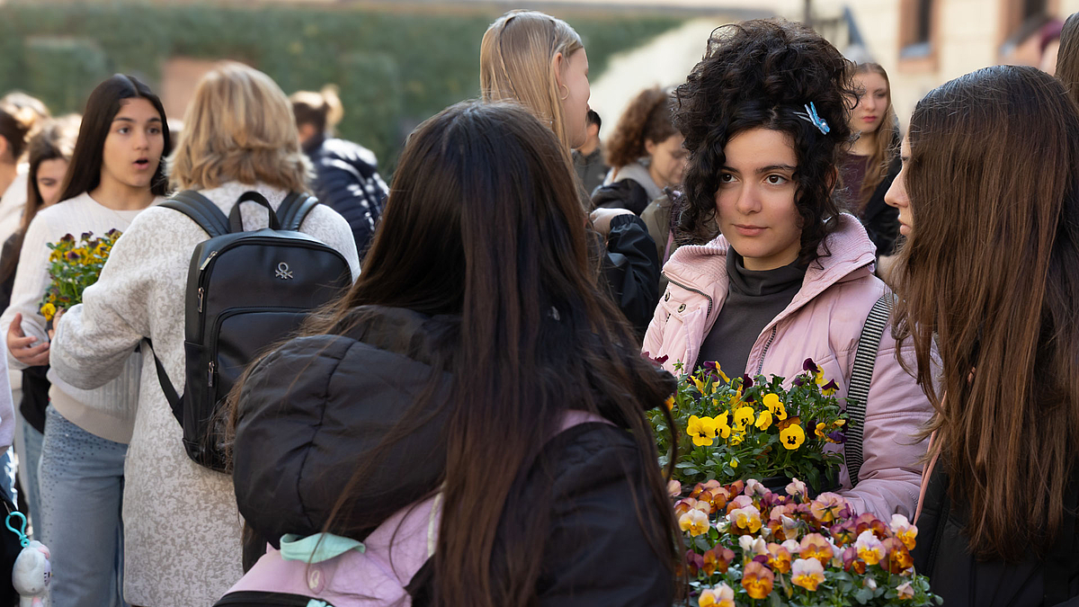 Junge weibliche Personen mit blühenden Topfpflanzen.
