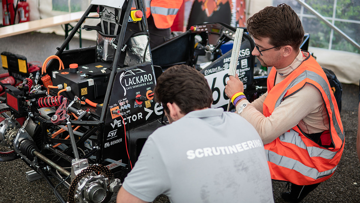 Zwei männliche Personen knieen vor der nicht verkleideten Antriebseinheit des Rennautos.