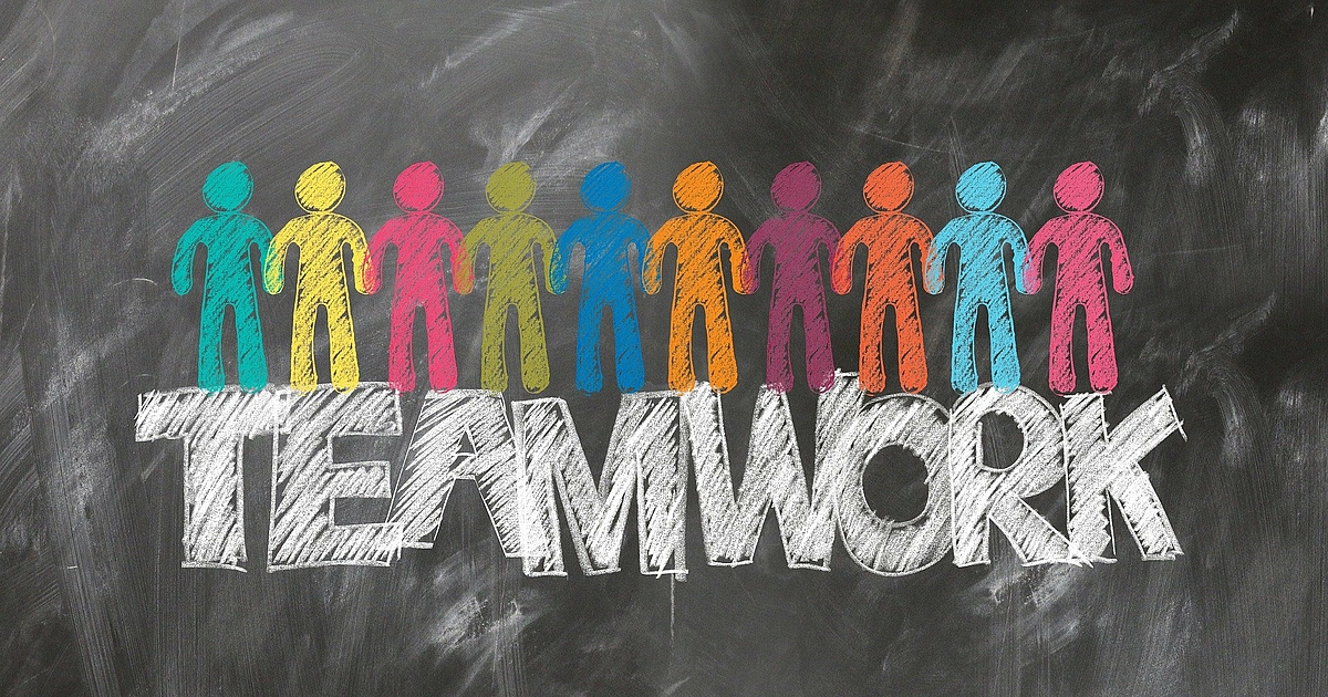 Teamwork Einer Tafel ist in großen Druckbuchstaben - TEAMWORK - zu entnehmen. Auf den einzelnen Buchstaben befinden sich Strichfiguren in den Farben grün, gelb, pink, kiwi, blau, orange, bordeaux, orange, hellblau und rosa.