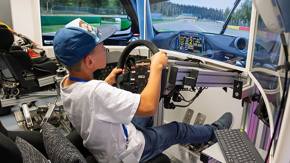 Ein kliner Junge inn em Rennsimulator. Er erreicht nur mit Mühe die Pedalerie, aber ist voll konzentiert.