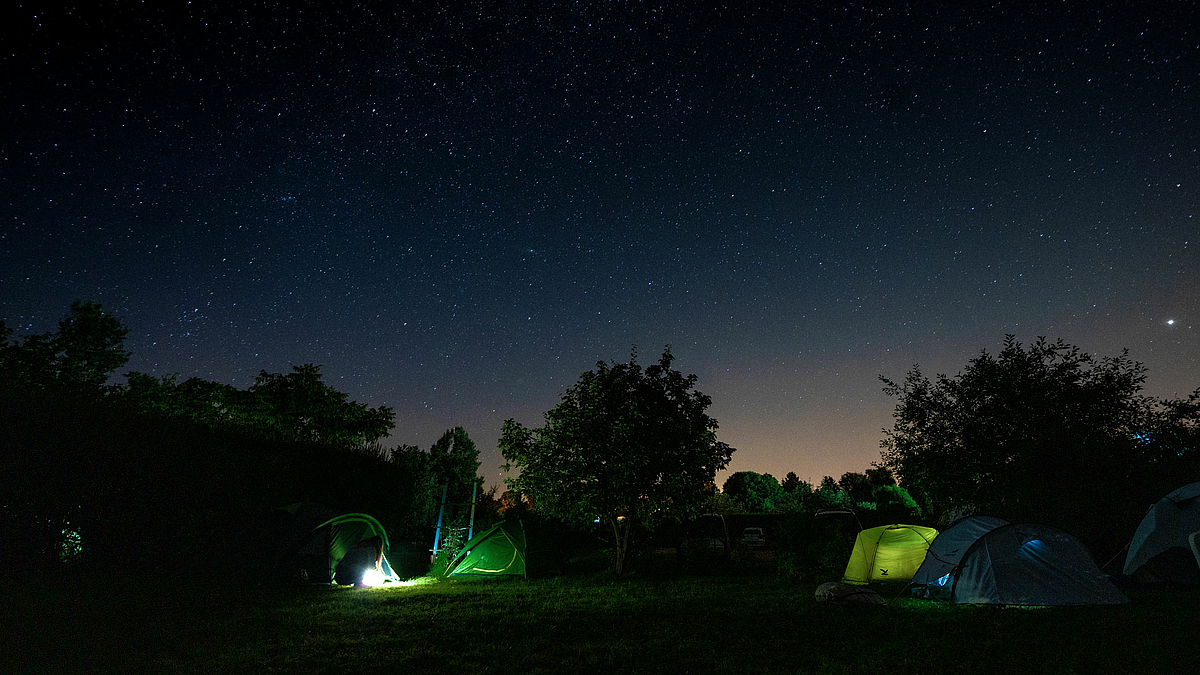 Das Foto zeigt Zelte unter dem Sternenhimmel. Aus den Zelten scheint Licht hindurch.