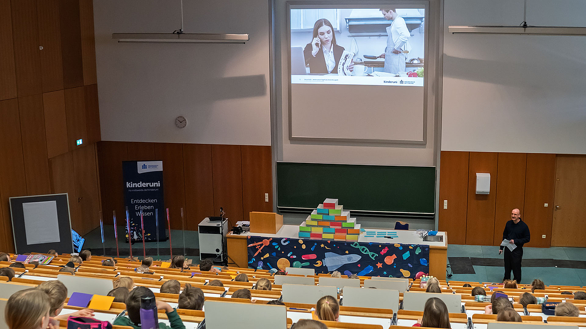 Selbe Einstellung wie zuvor, nur zeigt das jetzt vollständige Foto eine Frau im Anzug und einem Mann mit Schürze.