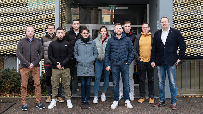 Acht männliche und zwei weiblichen Personen haben sich vor dem Eingang eines Gebäudes zum Gruppenfoto aufgestellt.