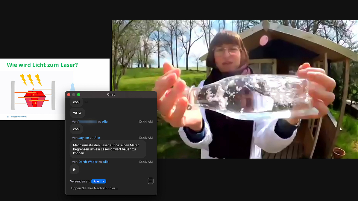 Das Foto zeigt einen Screenshot mit einer Folie links und der Überschrift: „Wie wird Licht zum Laser", daneben das Livekamerabild der Dozentin vor ihrem Gartenhaus, die eine mit Wasser gefüllte Flasche horizontal in die Kamera hält und offensichtlich hin und her schwenkt. Zusätzlich ist ein Chat-Fenster zu sehen, in dem sich Teilnehmende der Vorlesung über die Realisierung eines Laserschwerts austauschen.