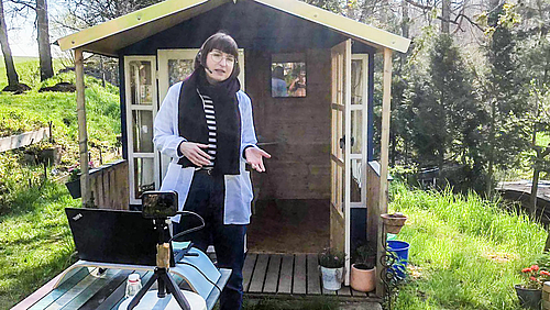 Kinderuni-Dozentin Dr. Inga-Maria Eichentopf hält die Vorlesung mit vielen Experimenten live aus ihrem Garten. (Foto: privat) Das Foto ziegt die Kinderuni-Dozentin Inga-Maria Eichentopf mit weißenem Kittel in ihrem Garten. Im Vordegrund ist eine Kamera zu sehen, im Hintergrund das Gartenhaus, das als Labor dient. e