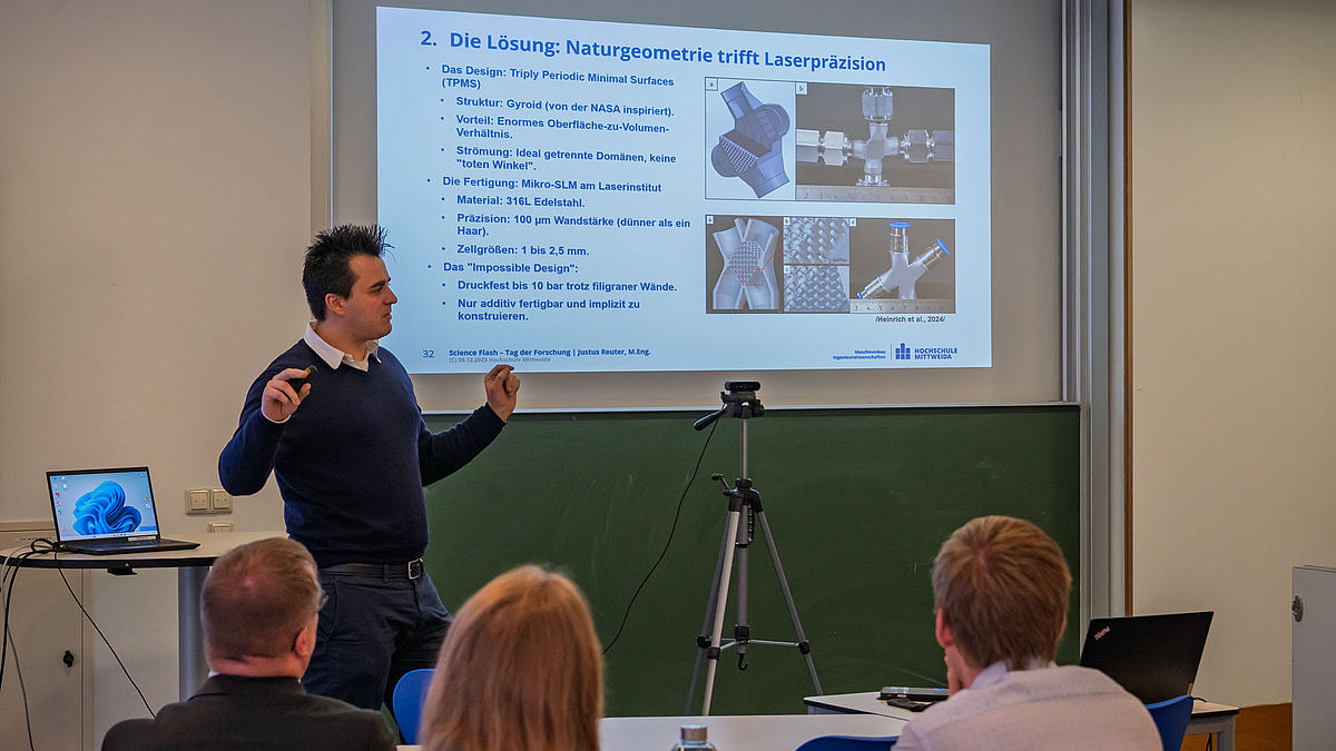 Männliche Person vor projizierter Powerpointpräsentation. Im Vordergrund Köpfe des Publikums von hinten.