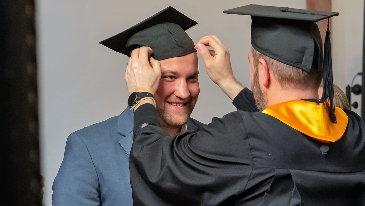 Professor im Talar setzt Absolvent Hut auf.