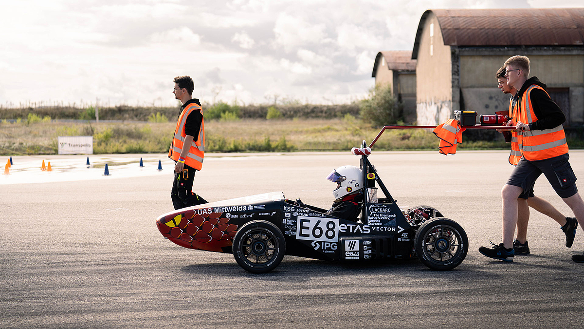 Rennauto mit Fahrer begleitet von drei männlichen Personen.