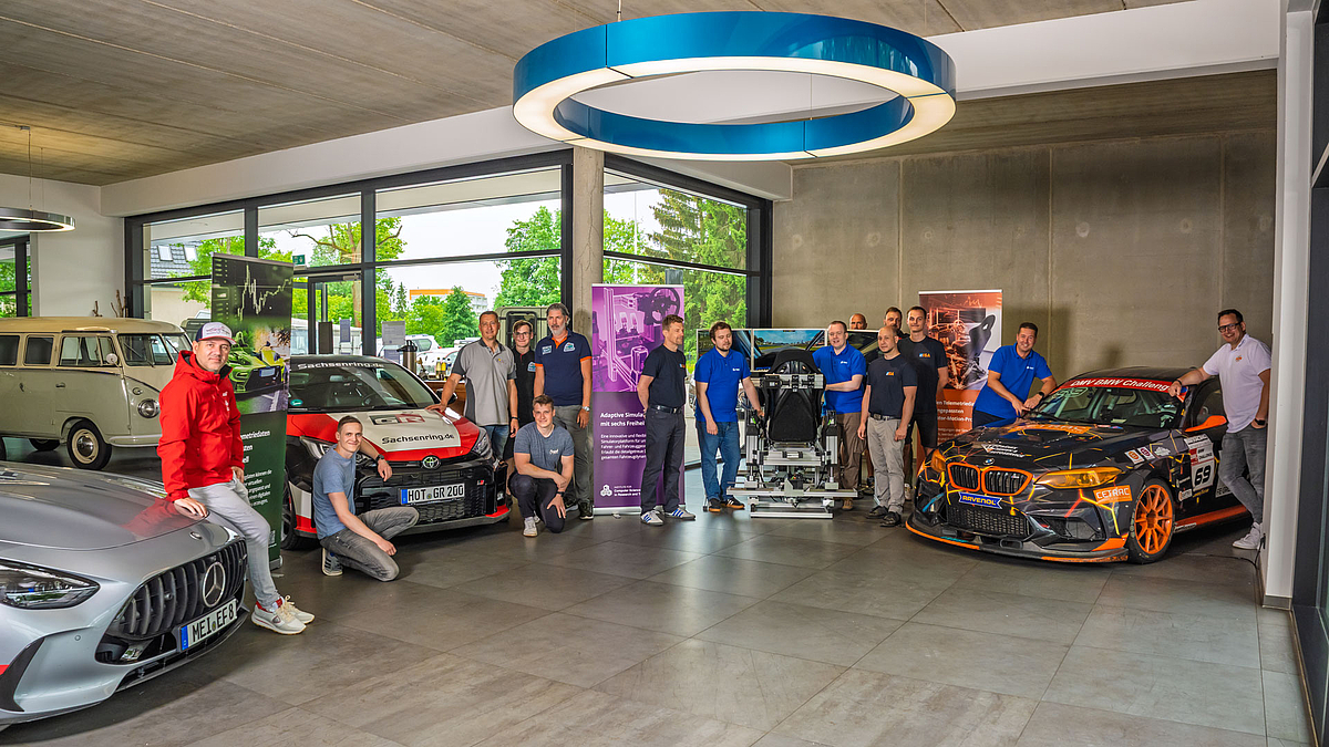 Sieben Sachsen: Vertreter der InnoTeam-Partner im Chemnitzer Auto Zentrum Nord. (Foto: Helmut Hammer) 15 männliche Personen stehen im Showroom eine Austohaus um drei sportliche bzw. Rennfahrzeuge.
