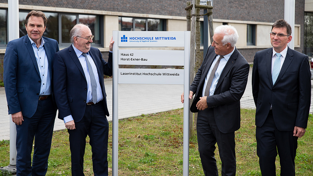 Mittweidas Oberbürgermeister Ralf Schreiber und HSMW-Rektor Ludwig Hilmer stehen links vom Schild mit der Aufschrift "Horst-Exner-Bau", rechts davon haben sich Horst Exner und Alexander Horn zum Gruppenbild aufgestellt.