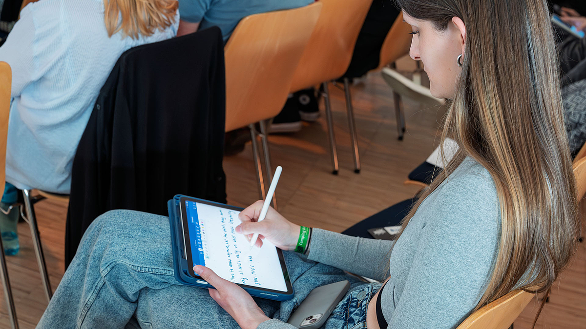 Blick über die Schulter einer Frau, die auf ihrem Tablet Notizen macht.