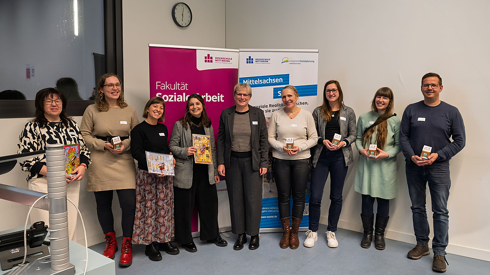 Das Fachtteam des Fachtages Gruppe aus acht weiblichen und einer männlichen Person am unteren Ende des Hörsaals vor Rollups mit "Fakultät Soziale Arbeit" und "Mittelsachsen Sozial"