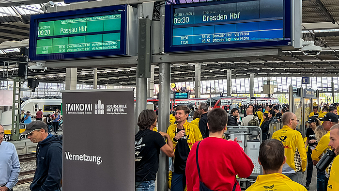 Menschen, darunter viele Sportler im gelben DHL-Trikot an einem Bahnsteig.