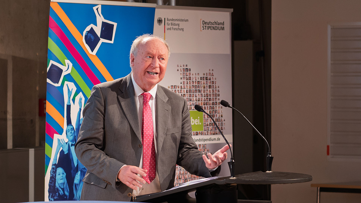 Männlicher Redner am Pult. Hinter ihm Rollups mit Deutschlandstipendium-Motiven.
