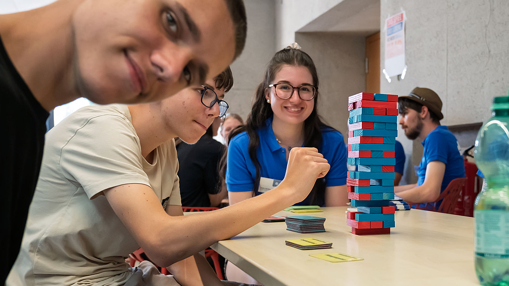 Drei junge Personen an einem Tisch bei einem Jenga-Spiel.