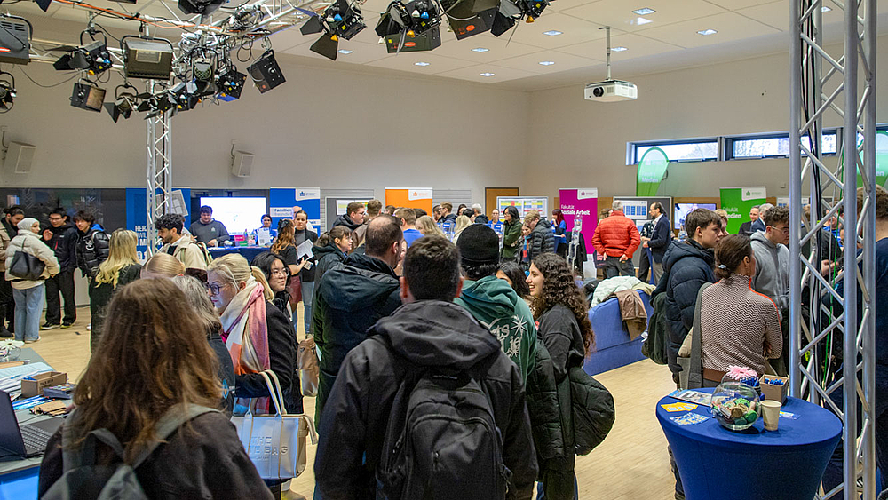 Blick in großen Raum mit vielen Besuchenden an Infoständen.