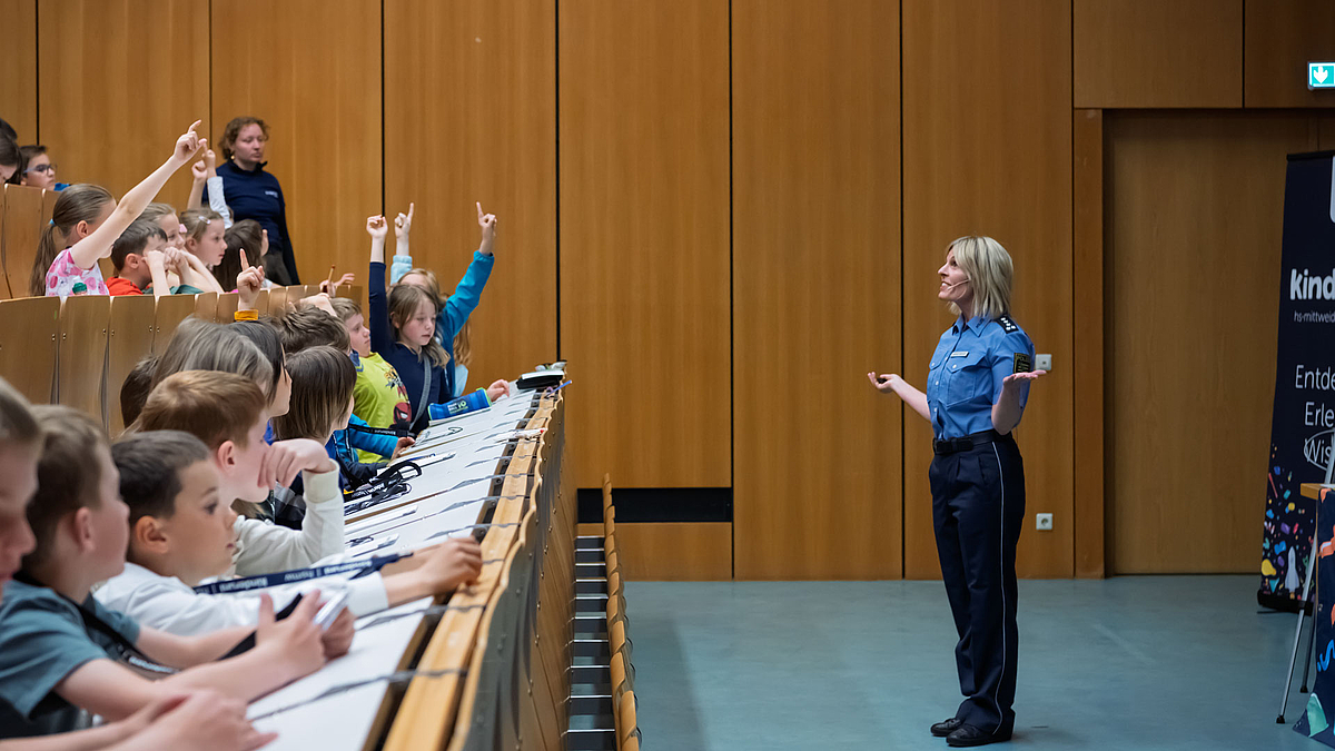 Polizistin spricht vor einer Gruppe von Kindern in einem Hörsaal, Kinder melden sich, um sich zu beteiligen.