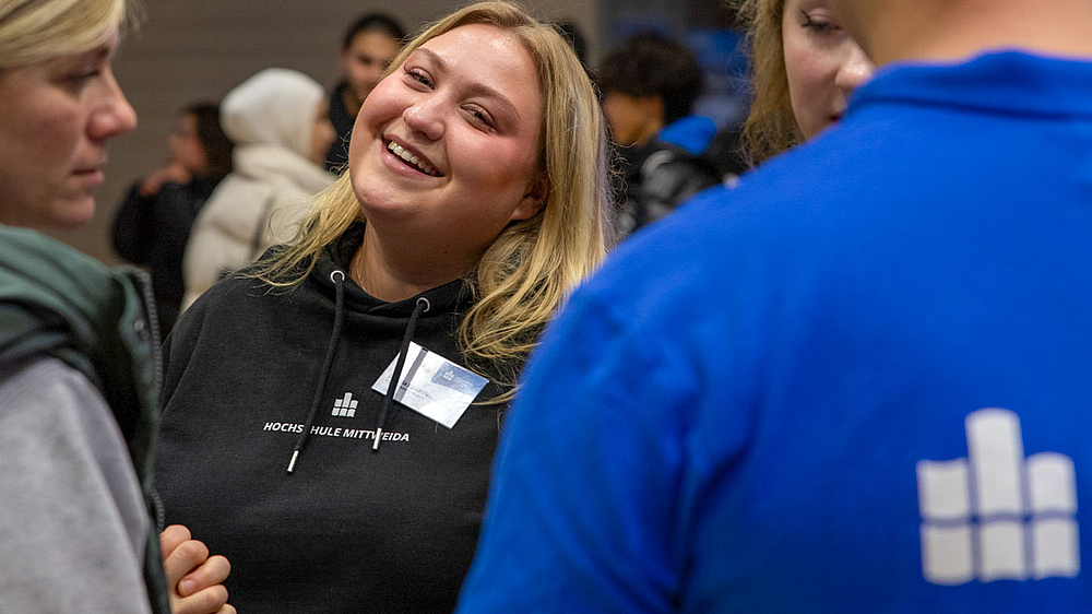 Lachende junge Frau mit rotem HSMW-Hoodie im Gespräch.