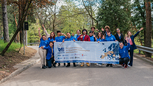 15 Studierende halten auf einem Gruppenbild einen großen Mesh-Banner mit einem Aufdruck der Hochschulallianz EURECA-PRO in die Kamera.