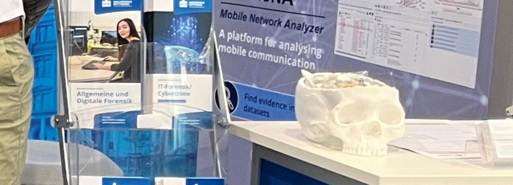 Fünf Personen stehen an einem Messestand; ein Torso trägt ein beschichtetes Shirt